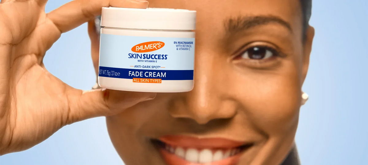 Close up of woman's face with her holding a jar of Palmer's Skin Success Fade Cream in front of one eye